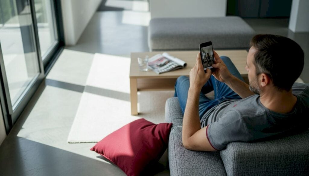 Ένας άνδρας κάθεται αναπαυτικά στον καναπέ και παρακολουθεί ένα σύντομο βίντεο στο κινητό του.