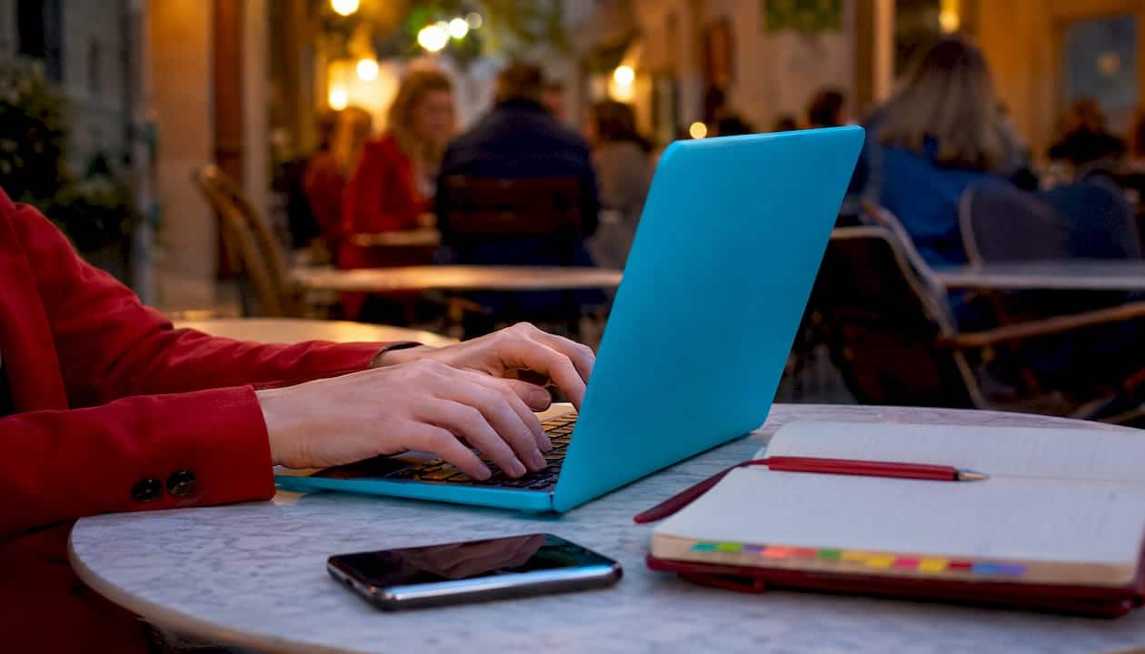 Δάχτυλα πληκτρολογούν στον υπολογιστή, δίπλα ένα σημειωματάριο κι ένα κινητό.